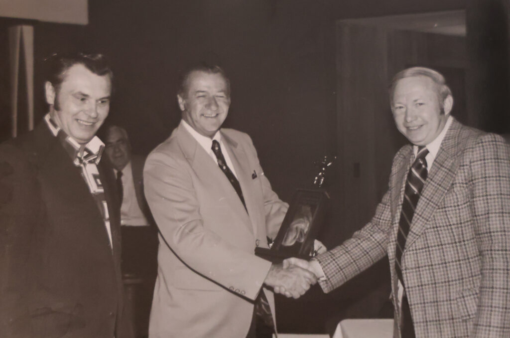 Bernie and Nick receive an award for being the first distributor to reach one million dollars. The award is presented by Gene Duke.